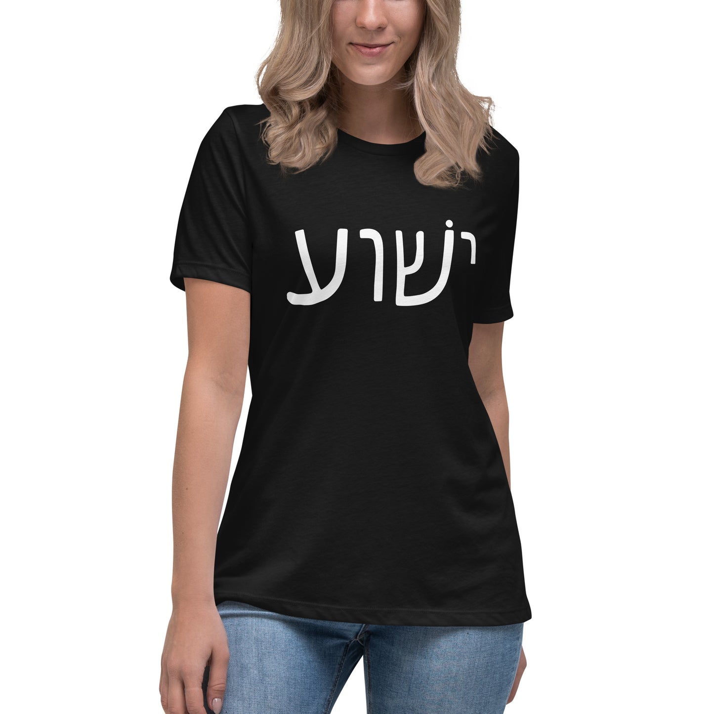 A person with long blonde hair is wearing a black Yeshua - Womens T-Shirt by deusdesign, featuring white Hebrew script on the front. They stand against a neutral background, paired with classic blue jeans.