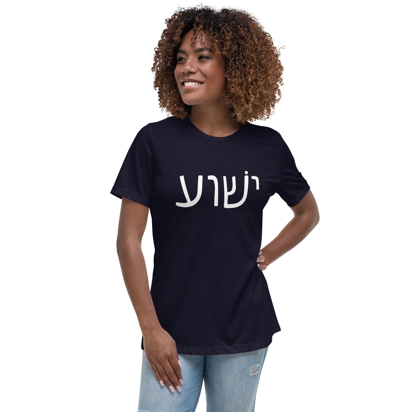 A smiling woman with curly hair confidently wears a black Yeshua - Womens T-Shirt by deusdesign, featuring white Hebrew text. This stylish piece enhances her vibrant energy against the plain white backdrop.